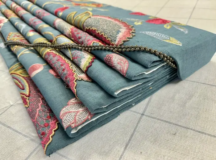 Folded Colefax & Fowler linen in teal with a colourful embroidered floral and a bead-chain pull