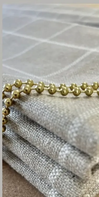 A folded oatmeal herringbone Ian Mankin Roman blind with a bead chain