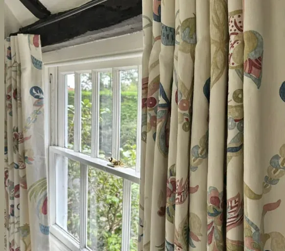 Cartridge-pleat Titley & Marr curtains in a soft multicoloured floral at a beamed cottage window
