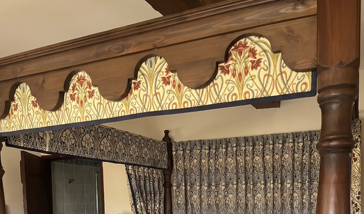 A shaped, pleated pelmet crowning a four-poster bed