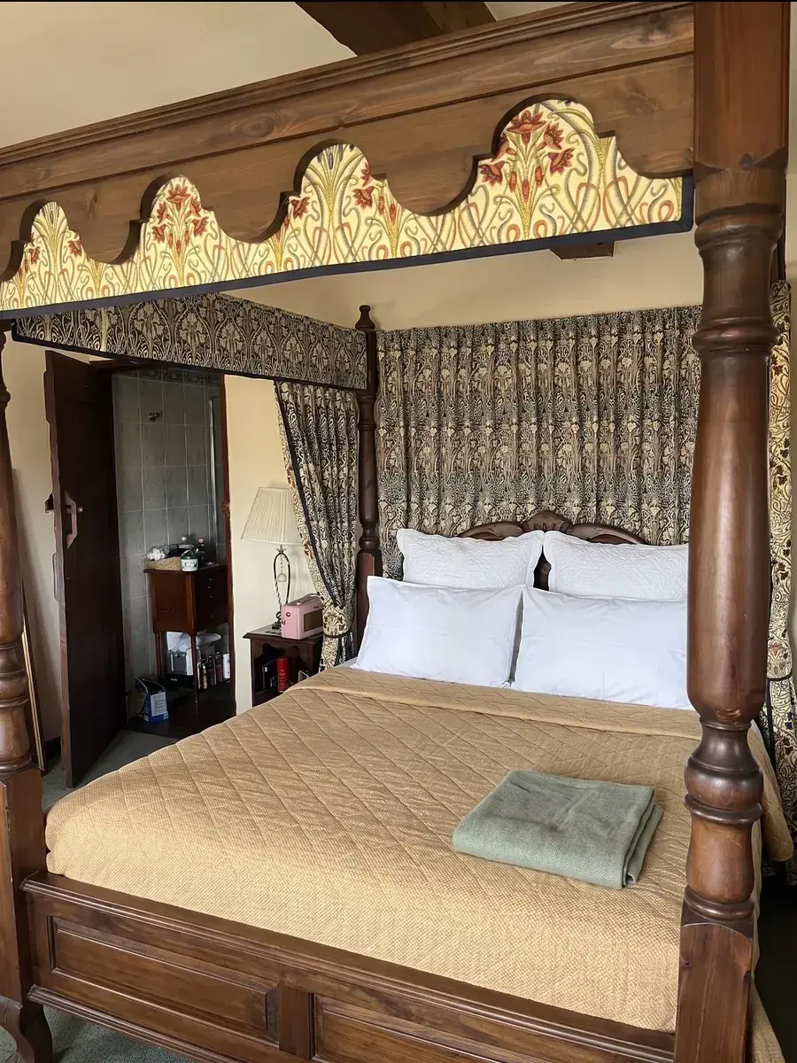 A four-poster bed dressed with curtains and a shaped, pleated pelmet